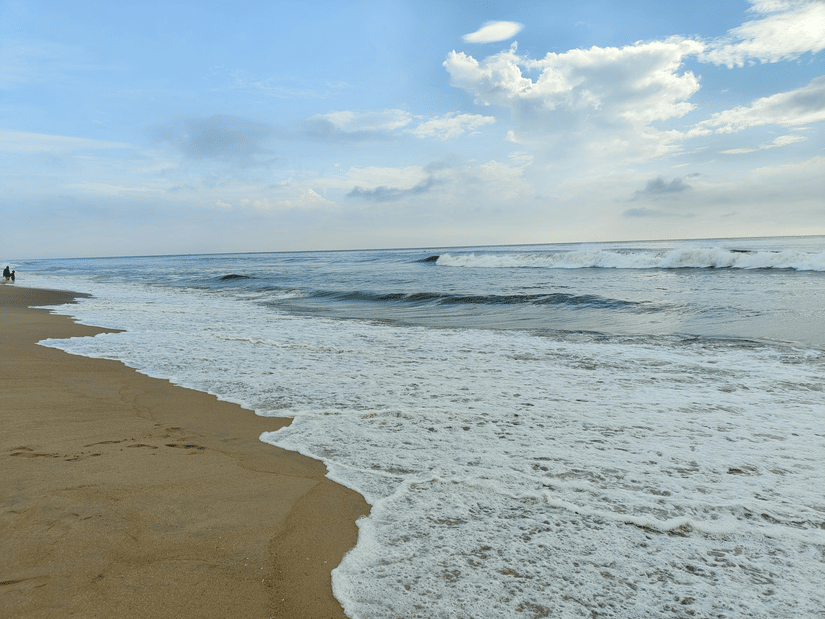 A view from the shoreline of Elliot's Beach, also known as Besant Nagar Beach, with foamy water overlapping the shore and clouds in the distance.