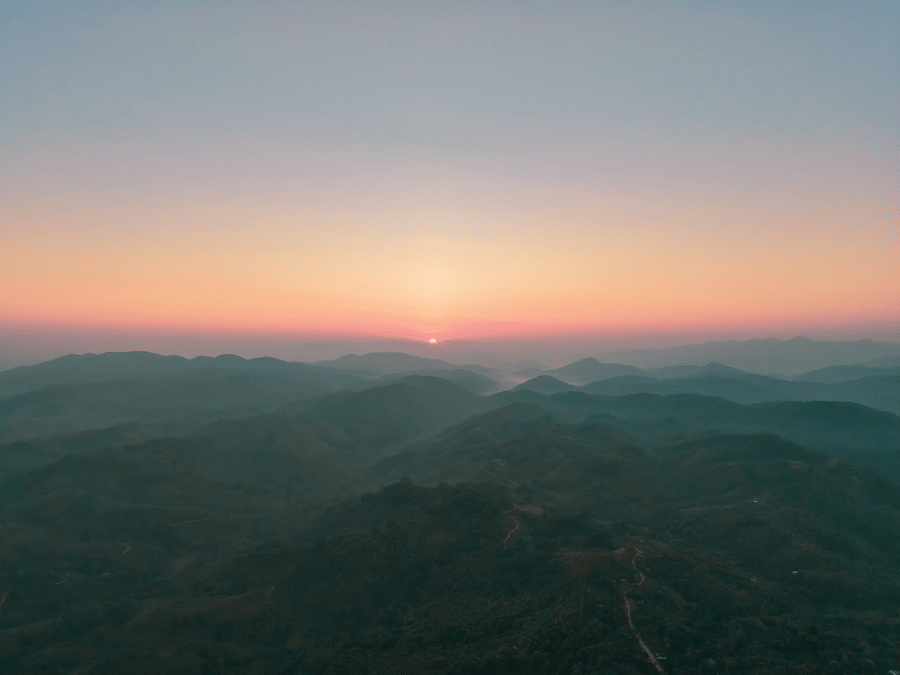 A wide landscape shot of a sunset over multiple layers of hazy blue and green mountain ranges | Abad Silvermist, Vagamon