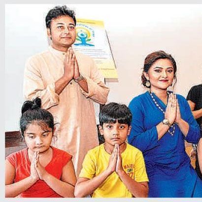 International Yoga Day celebration at Vedic Village Spa Resort, featuring children and adults sitting together with praying hands.
