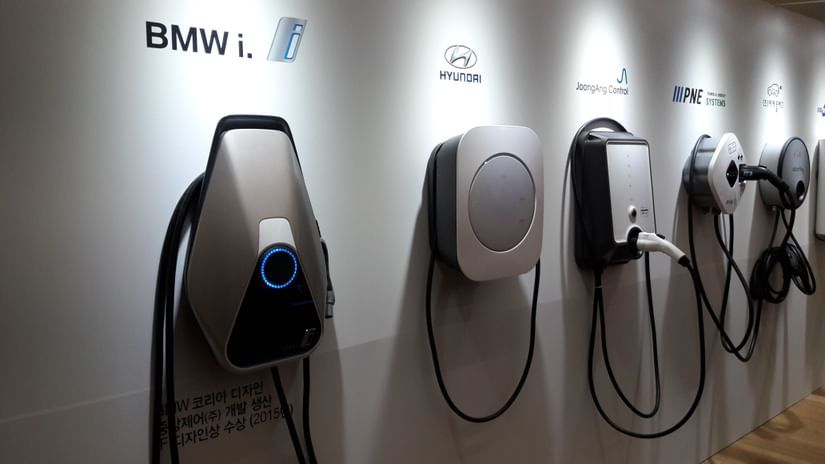 An overview of a wall with many types of EV chargers hung on it and spotlights on top of the chargers.