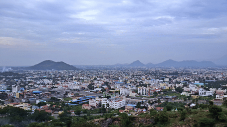 Panoramic cityscape with houses and buildings spread across the valley and hills.
