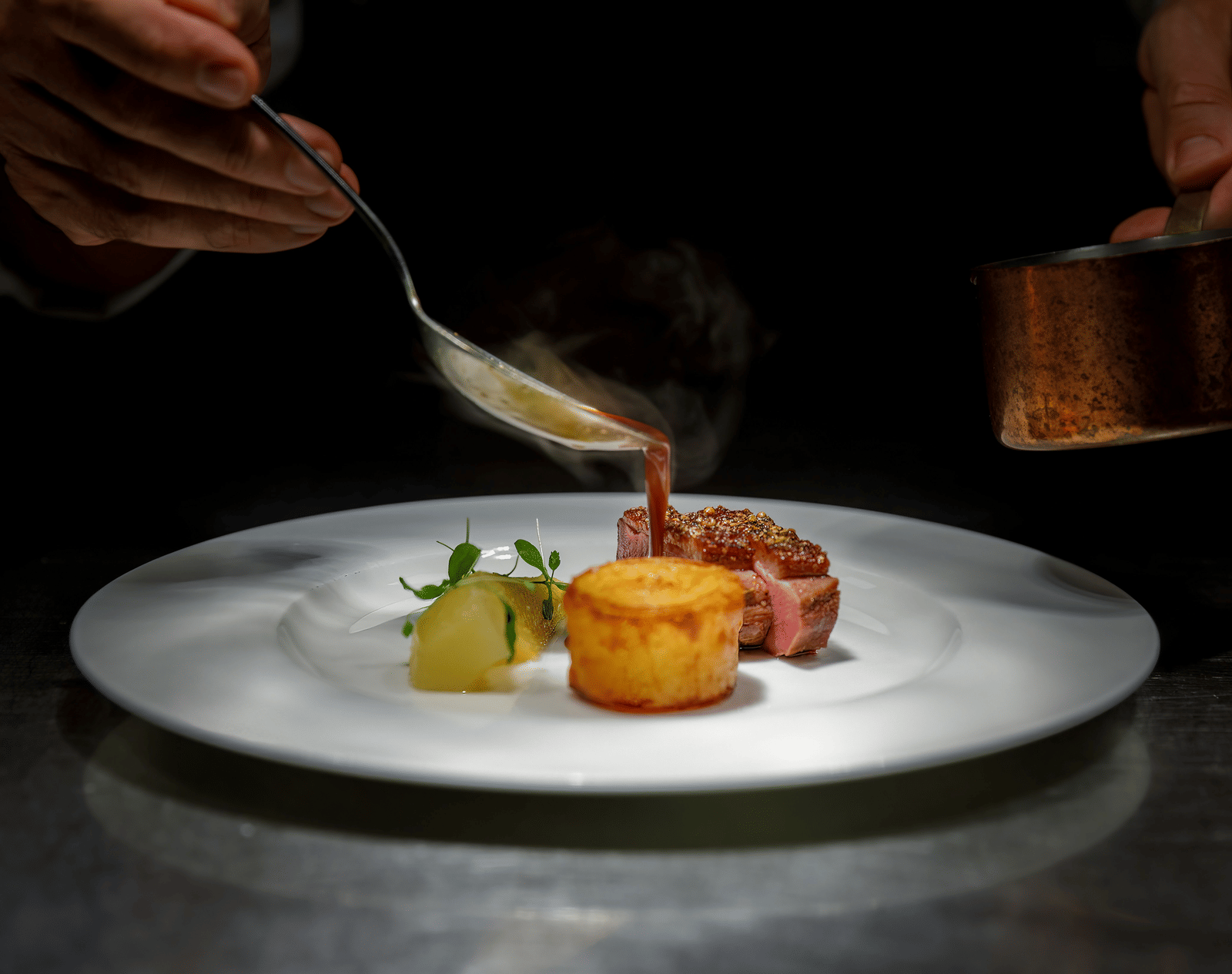A professional culinary presentation showing sauce being drizzled onto a small, artistic dessert or appetiser.