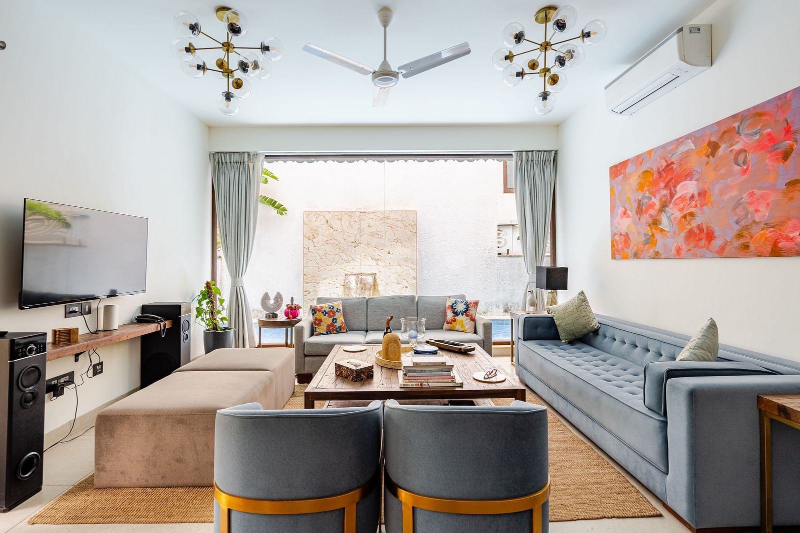 Living area at Lindsay Manor with a grey sofa set, TV, ceiling fan, abstract wall art, and an open view to an outdoor space.