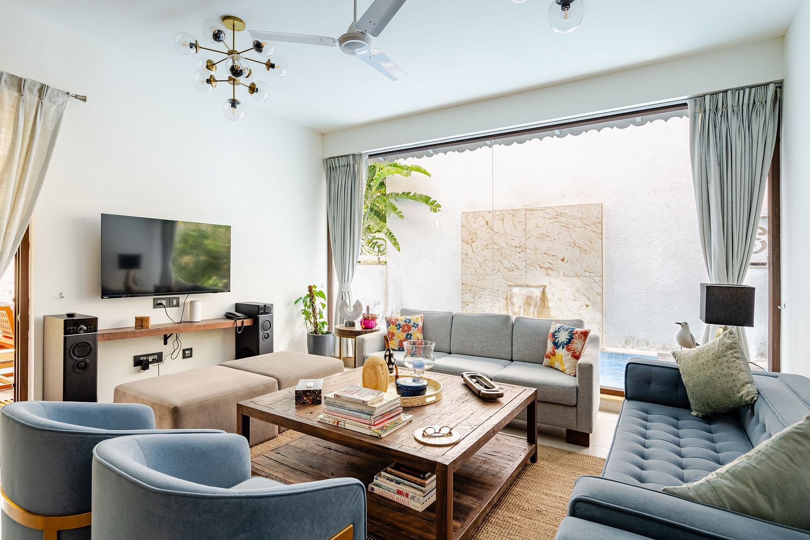 Modern living room with cosy sofas, a rustic wooden coffee table, wall-mounted TV, and large glass doors opening to a private water feature - Lindsay Manor