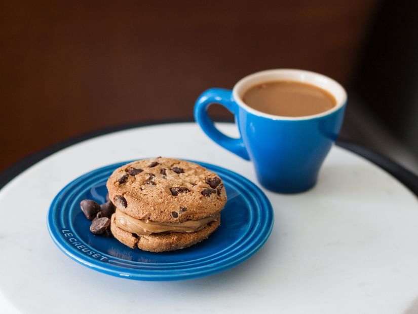 Two cookies stacked on a plate with chocolate pieces, accompanied by a cup of liquid.