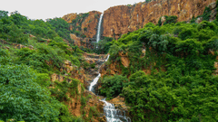 a waterfall winding down a mountainside with forest cover on either side