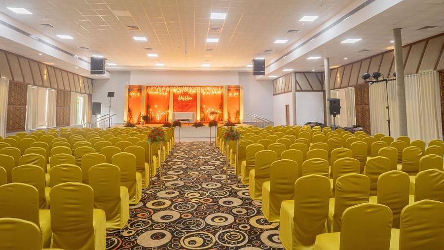 An image of a banquet hall with several chairs, speakers, cameras, and a stage set up on the front part of the hall- The Renai Cochin