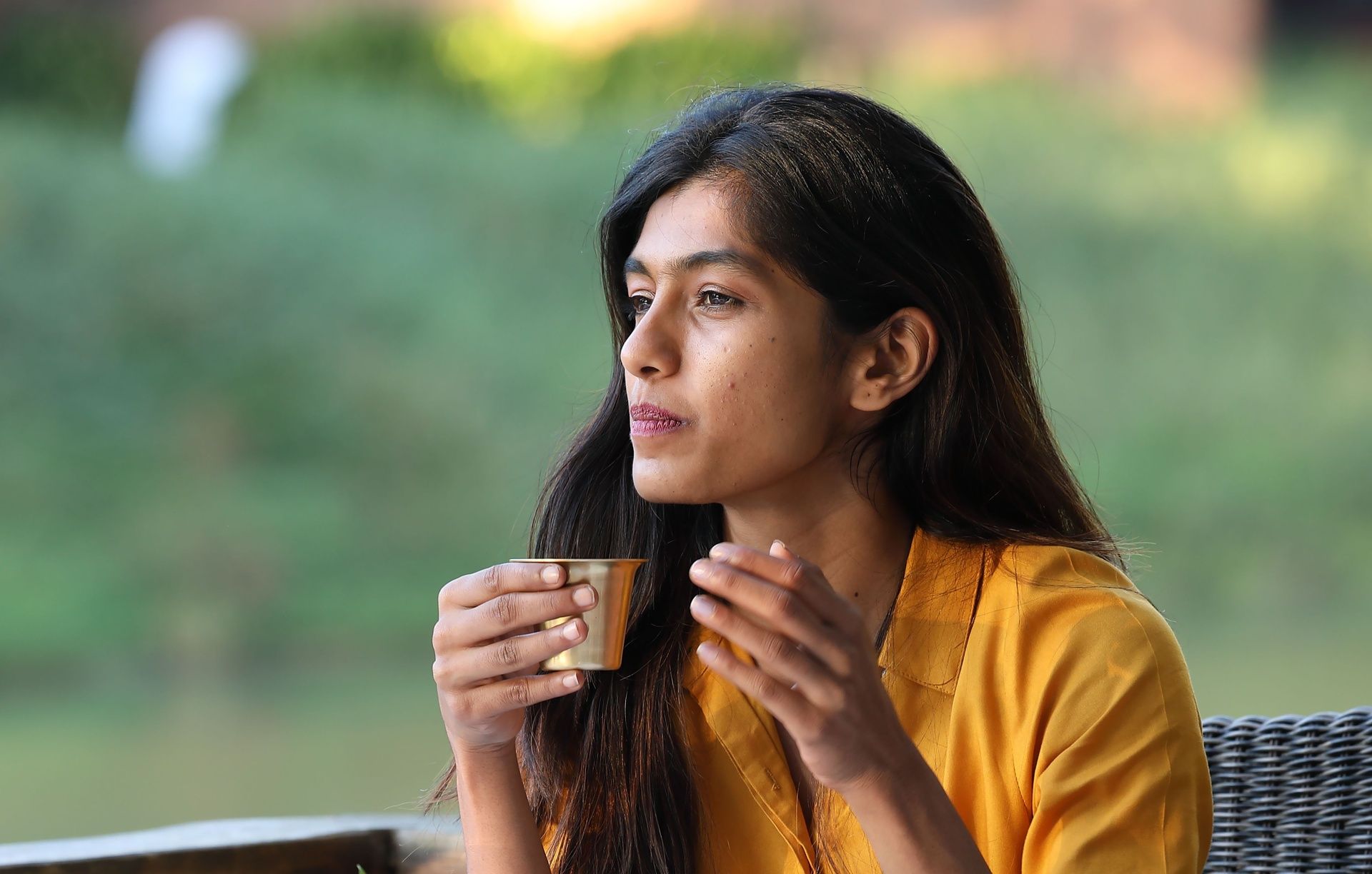 Woman in yellow holds a coffee Cup and looks outdoors.