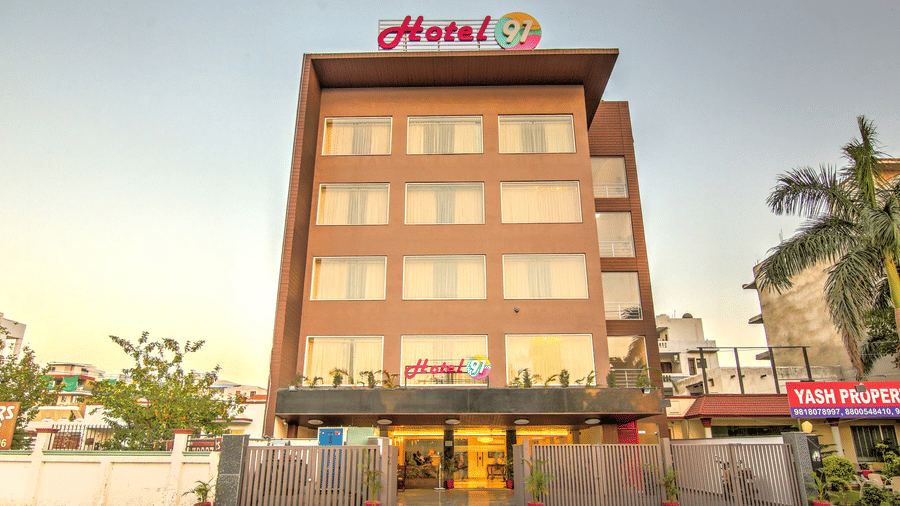 A full frontal view of the multi-storey hotel building featuring a modern brown and glass facade under a bright sky - Hotel 91 HUDA City Centre, Gurugram
