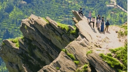 A bunch of people standing on the edge of a cliff with a hill on the backdrop.