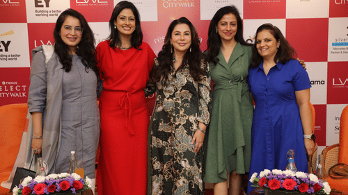 Group of five women posing in front of a branded backdrop at a Golf event, surrounded by floral decor.