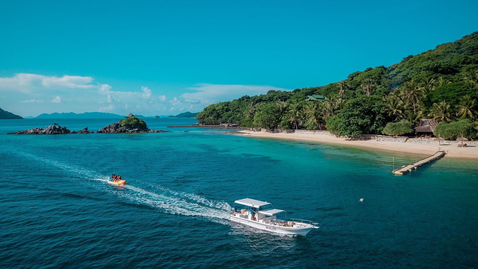 Speedboats on turquoise water near sandy beach and green hills at Flower Island Resort.