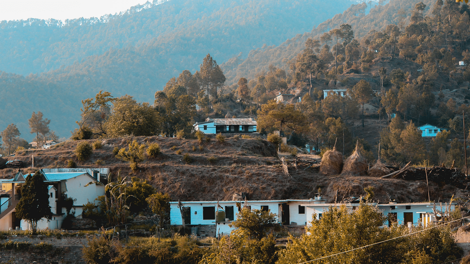 White houses built on various levels on a hill surrounded by land and trees with mountains in the background