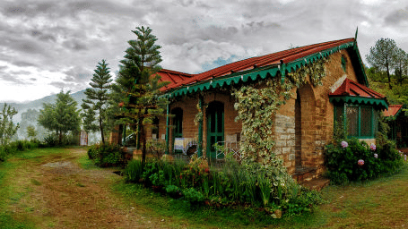 Facade of tower house during daytime surrounded by green trees and dark skies above.