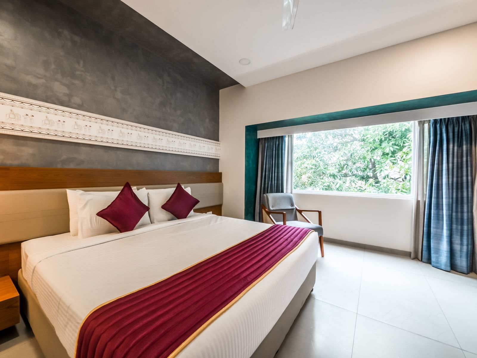A hotel bedroom with a large bed, a red and white bedspread, and a view of greenery outside | Shilton Hotels