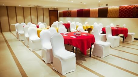 A well decorated banquet hall set up with round tables draped in red, ready for an event at Shilton Dee Cee.