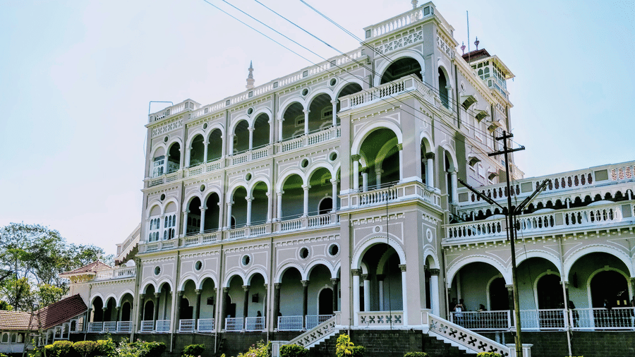 Aga Khan Palace rises above a neatly maintained garden, with elegant arches and balconies set against the sky.
