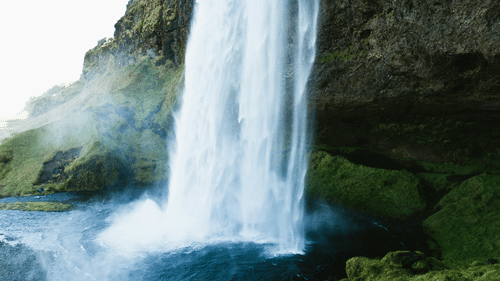Waterfall next to mossy rocks with mist rising from the waterfall in view