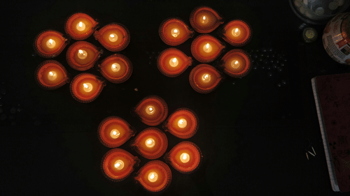 An aerial view of many lit diyas in a colourful pattern of seven