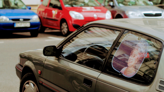 A low-angle, shallow-focus shot of a parked car with a sticker of a cartoon girl on its window. Other cars are behind it.