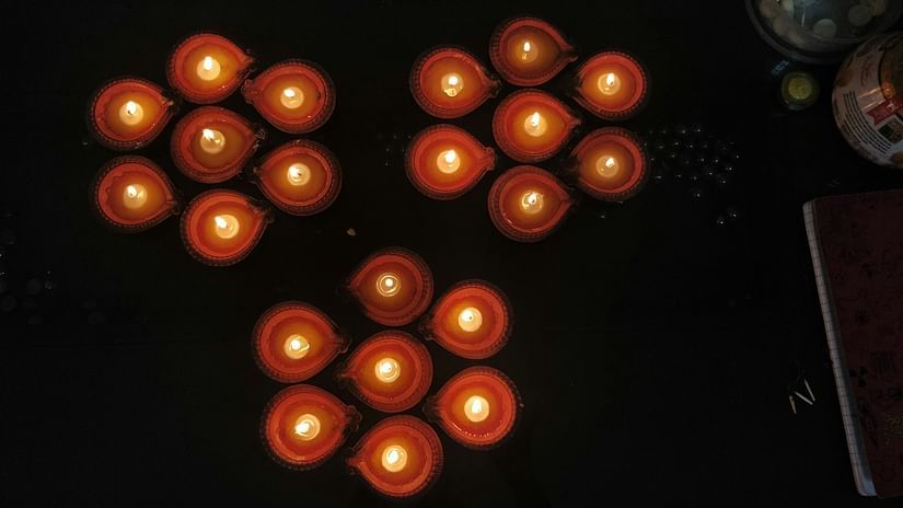 An aerial view of many lit diyas in a colourful pattern of seven