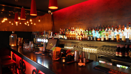 A sleek, modern bar area with red ambient lighting, a well-stocked back bar, and contemporary pendant lights.