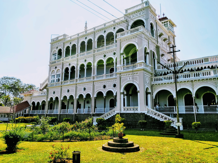 Aga Khan Palace rises above a neatly maintained garden, with elegant arches and balconies set against the sky.