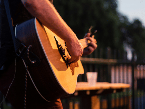 Close-up of a person playing an acoustic guitar at dusk with a soft-focus background, capturing a moment of musical passion.