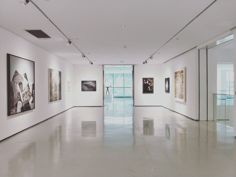 An interior view of an empty museum with paintings hung on the walls and spotlights above it.