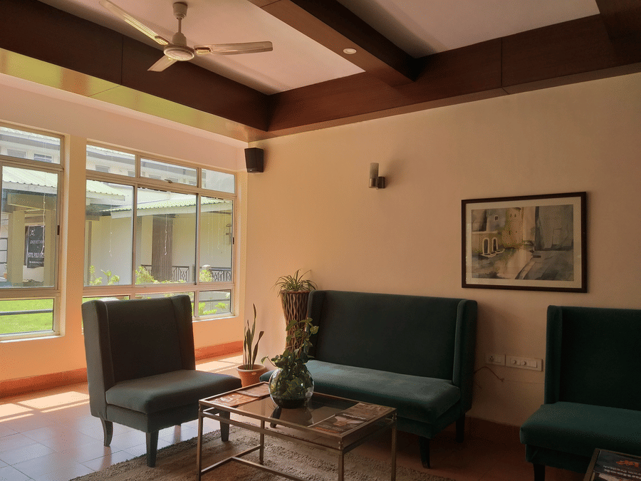 A cozy hotel lounge with green upholstered chairs, a coffee table, and a large window letting in natural light.