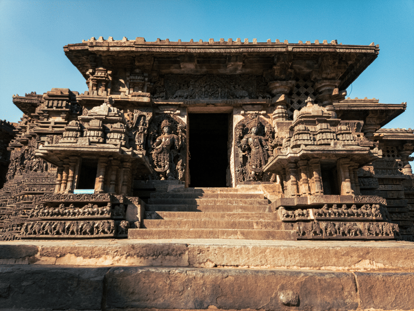 An overview to the entrance of Halebidu Temple with stone carved structures on either side of the door and steps leading to the entrance.