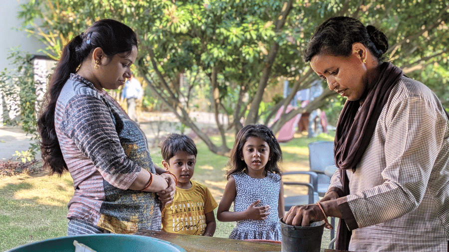 A group of people, including adults and children, gathered around bowls of soil or plants outdoors at The Golden Tusk, Jim Corbett