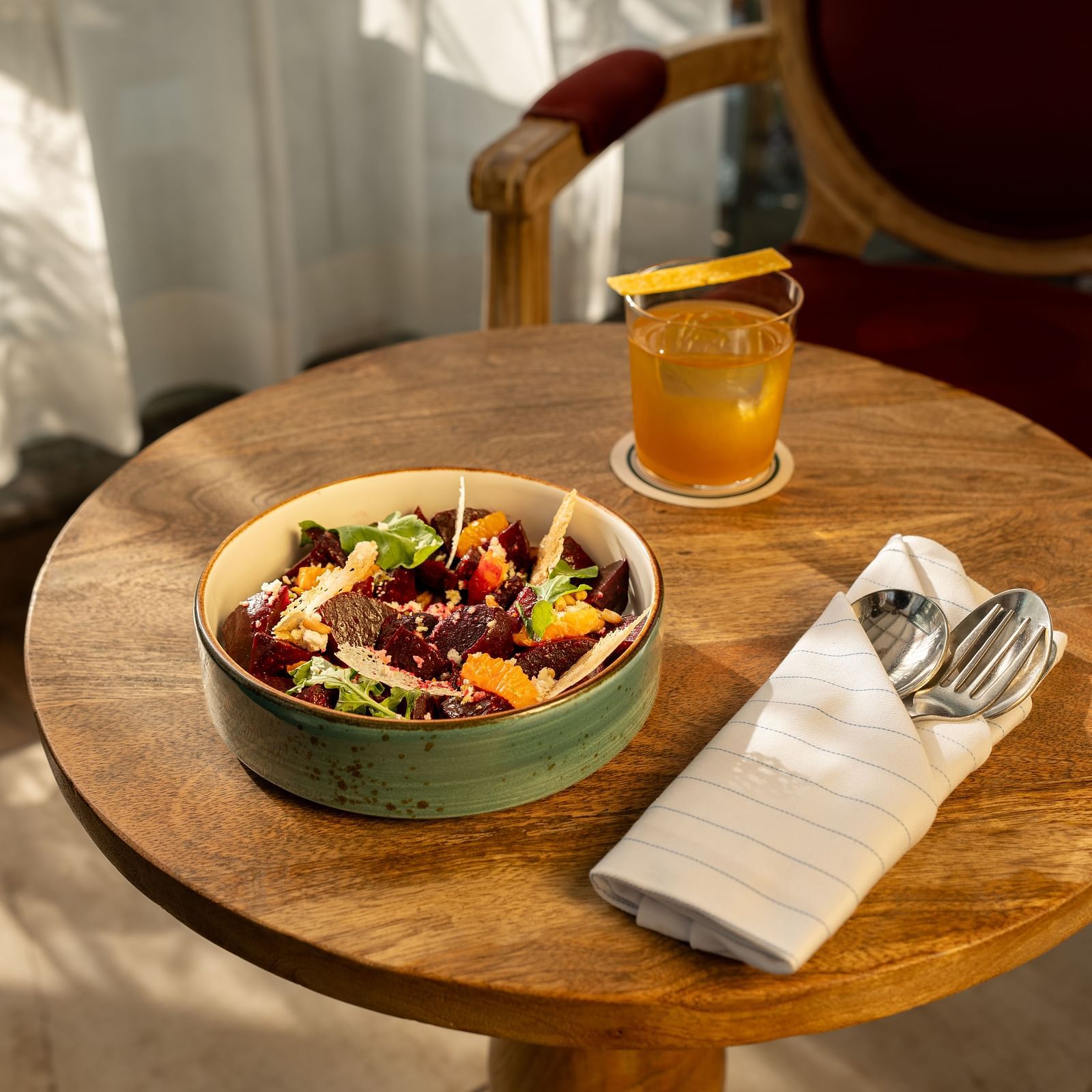 A bowl of vibrant beetroot salad and a cocktail served at Panna Vilas Palace, placed on a sun-drenched wooden table.