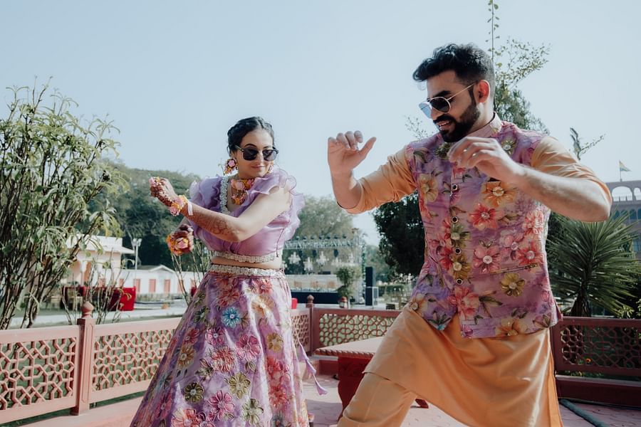 Bride and groom in colorful outfits dancing together during a haldi or sangeet ceremony on a terrace.