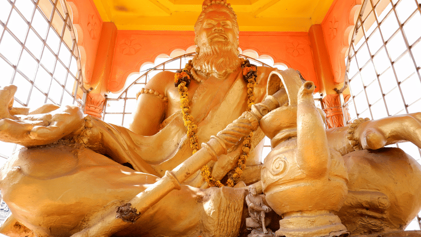 A statue of a seated figure holding a stringed instrument, with decorative elements around, placed inside a structure with railings and walls visible.