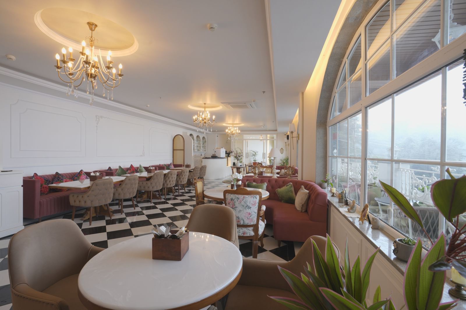 Sun-lit dining area with chandeliers, white tables, and cushioned booths - Mayfair Cafe & Suites, Dalhousie