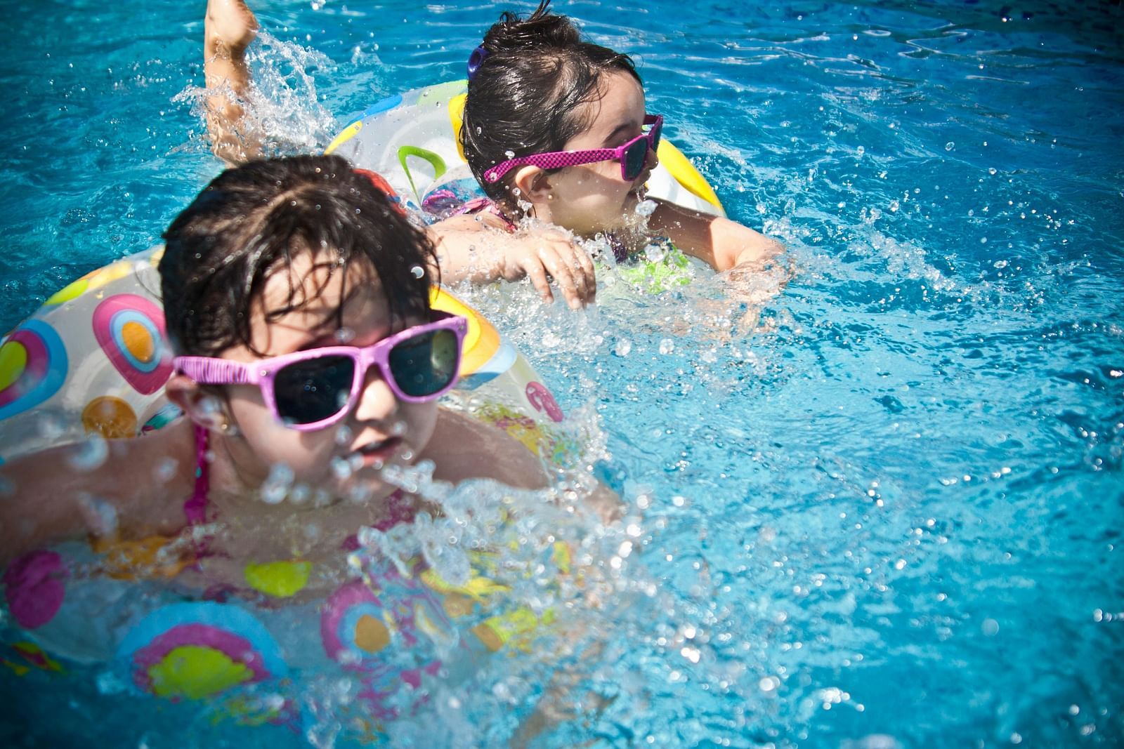 Two children wearing sunglasses, swimming in a pool.