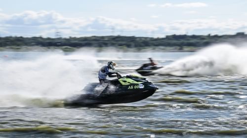 Person riding a jet ski at high speed, creating a spray of water on a sunny day.
