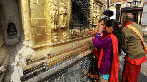 2 people standing near a temple wall sculpture while looking at carved figures on the stone surface.