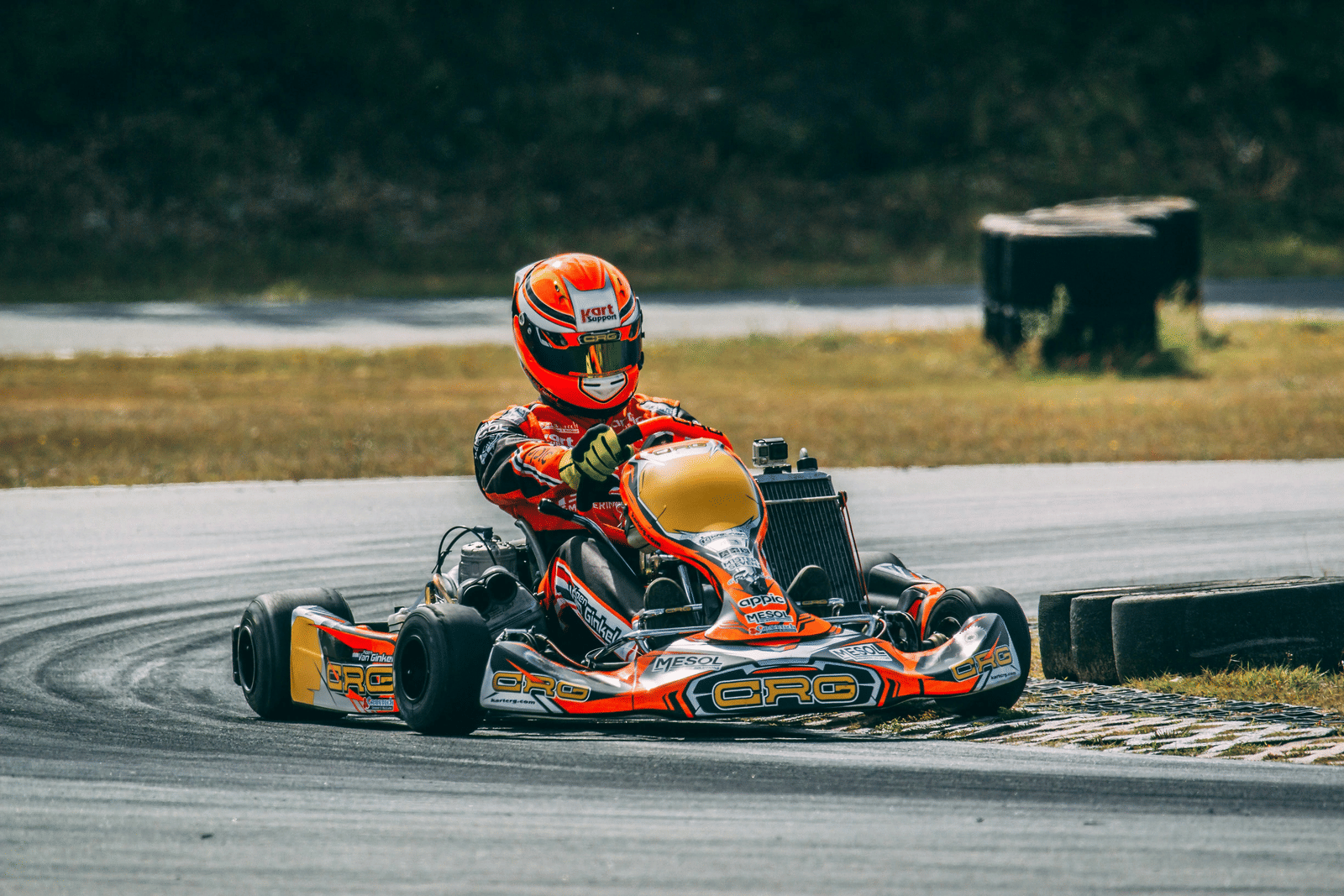 A racer in a helmet is driving a small go-kart on an outdoor race track.