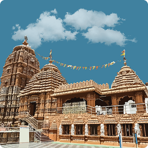 A detailed view of a temple with brown stonework and multiple spires, set against a blue, cloudy sky.