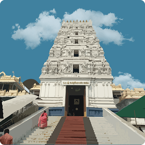 A white, ornate gopuram of a temple against a blue, cloudy sky.