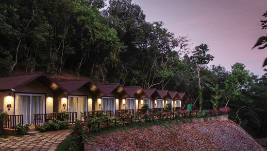 A night time view of our cottage illuminated by bright lamps with a serene pink sky in the background - Stone Wood Nature Resort, Gokarna