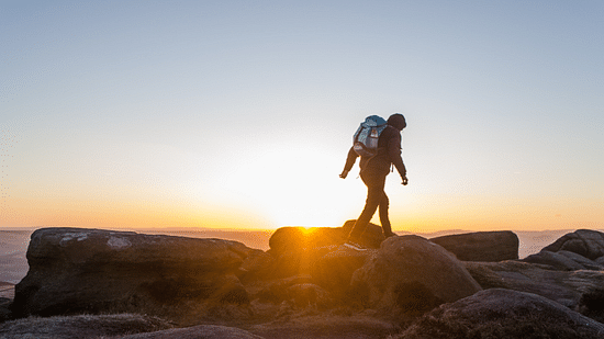 a person walking on rocks with a rucksack on his back and the sunset in the background
