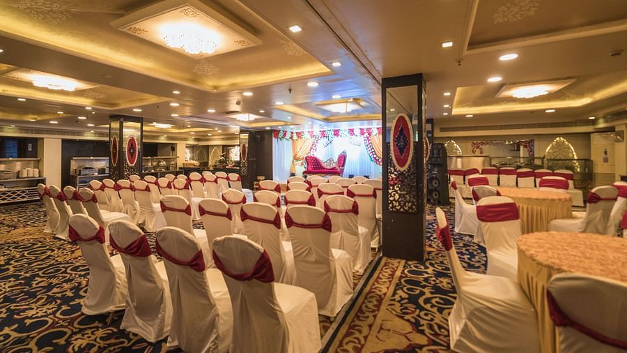 Maurya featuring rows of chairs with white covers and red sashes facing a stage area with draped fabric and lighting.