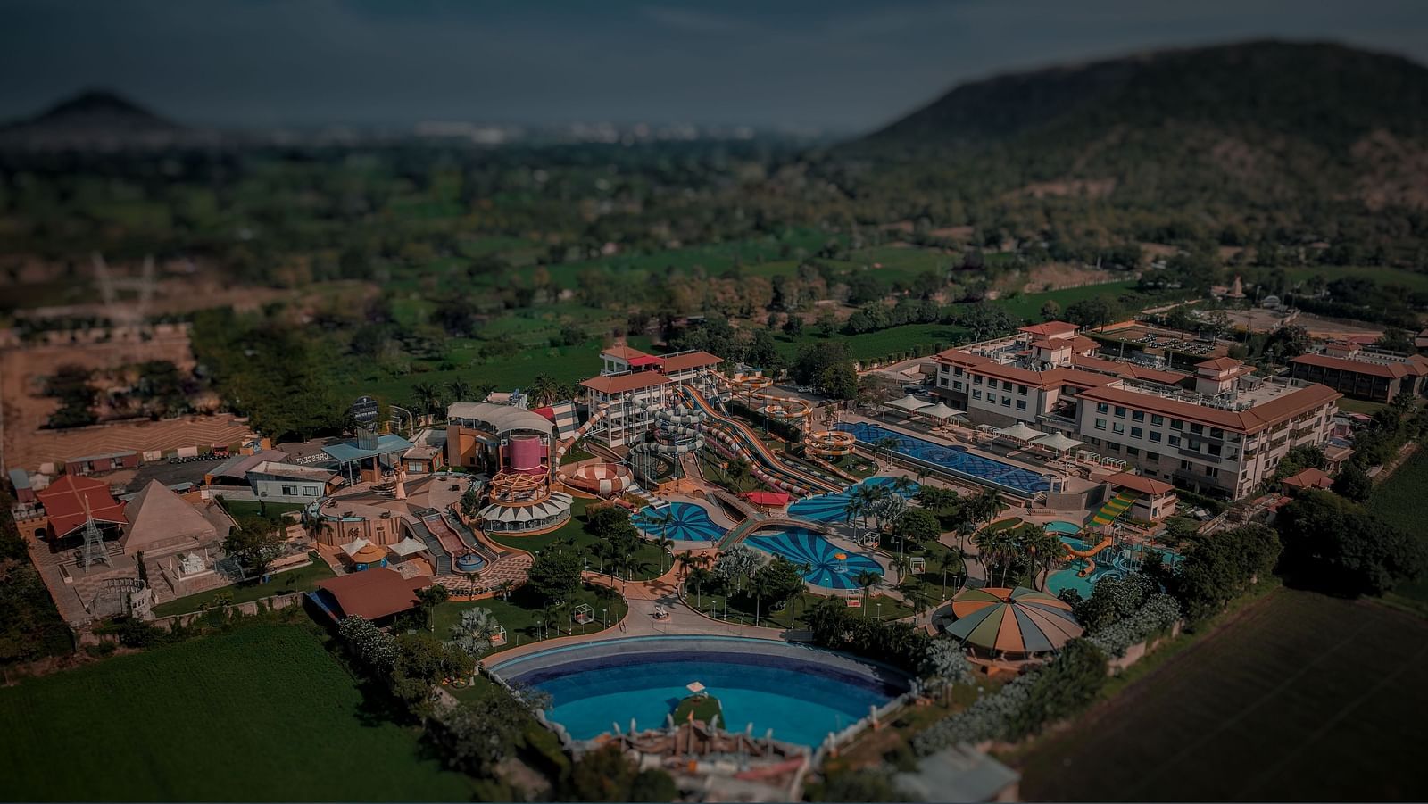 Aerial view of a large amusement park with roofed buildings, set against a dimly lit backdrop - Crescent Resorts