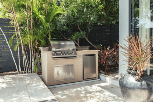 An outdoor kitchen setup with a grill is situated on a patio surrounded by lush greenery.