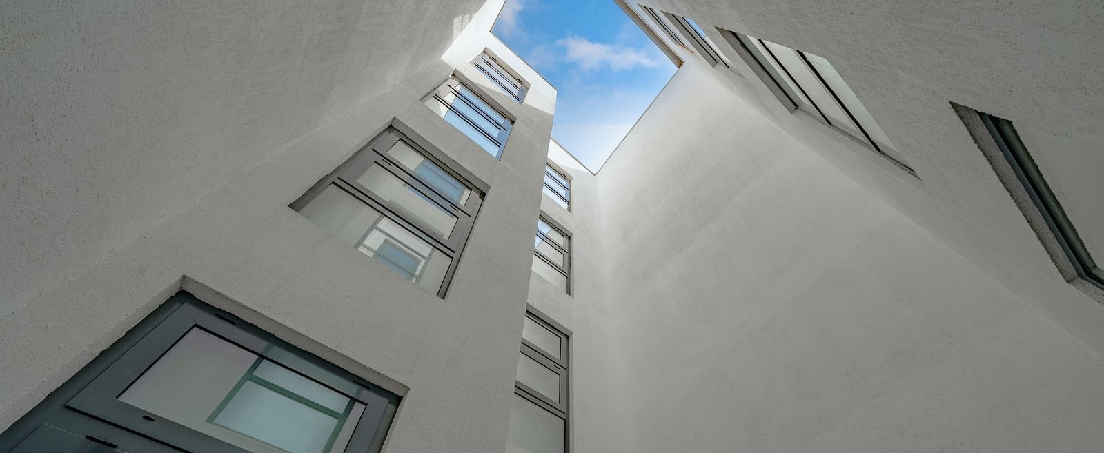 Upward view of a modern courtyard with tall white walls and large windows.- The Pelican Hotel, Accra
