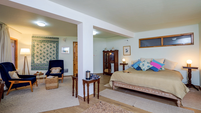 A spacious bedroom with a king size bed, 2 chairs, a table, and large windows.