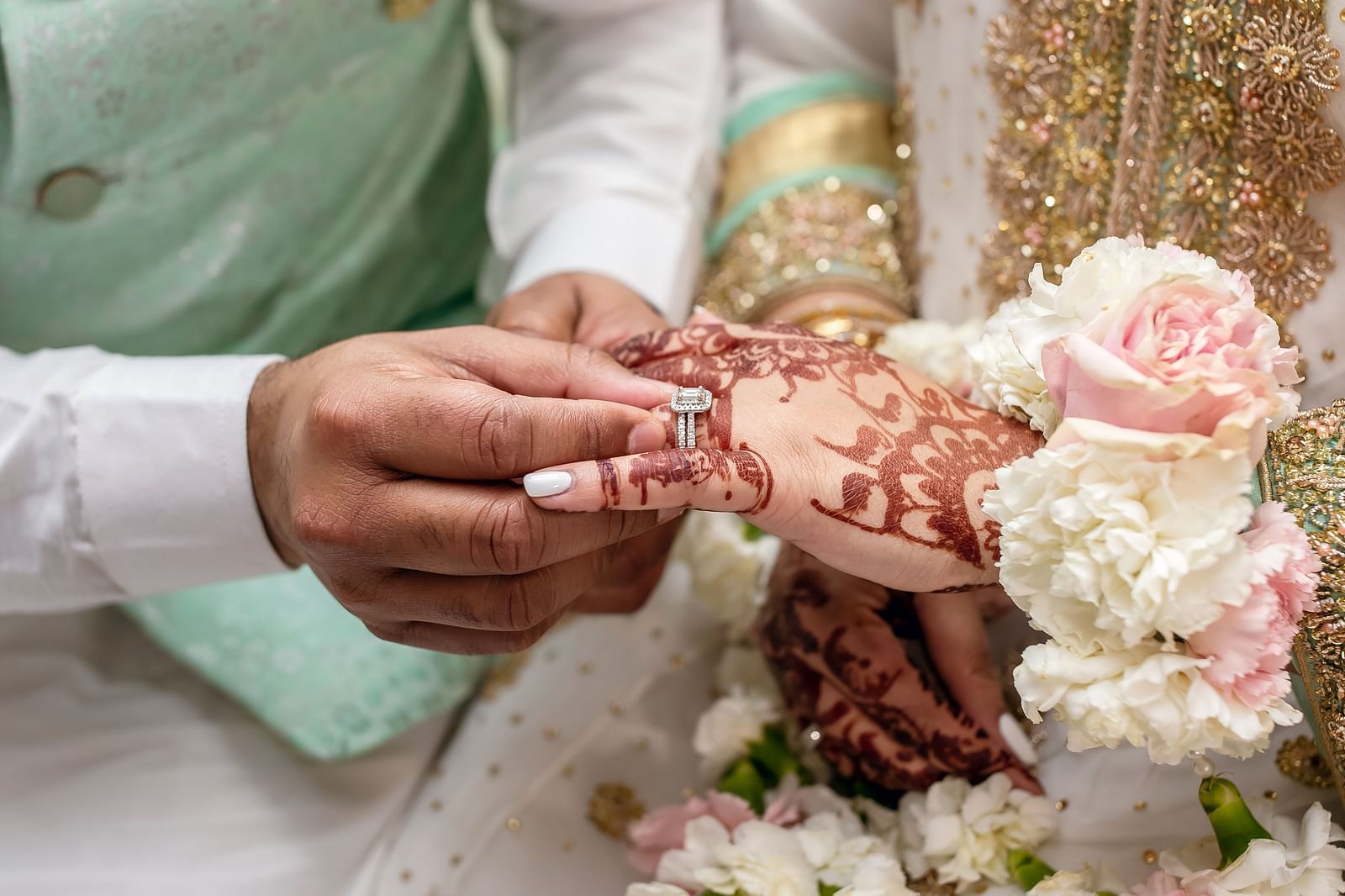 A close-up of a groom placing a diamond ring on the bride's hand during a traditional engagement ceremony.